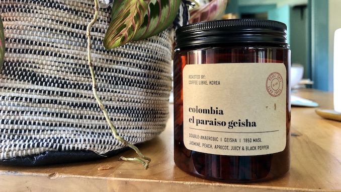 A small jar of double anaerobic coffee sitting next to a basket of plants.