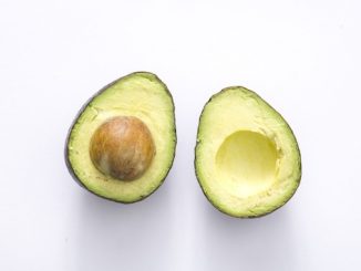 Two halves of an avocado amidst a white background.