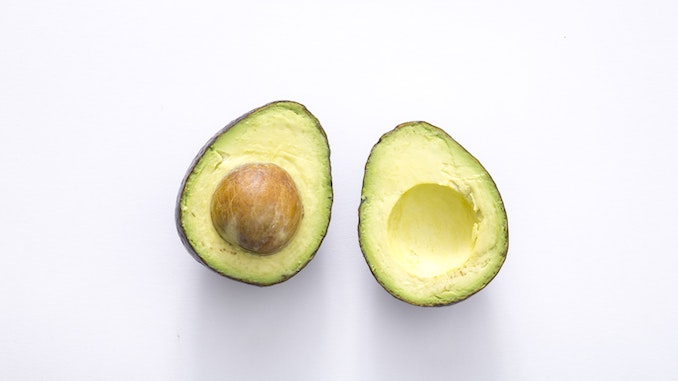 Two halves of an avocado amidst a white background.
