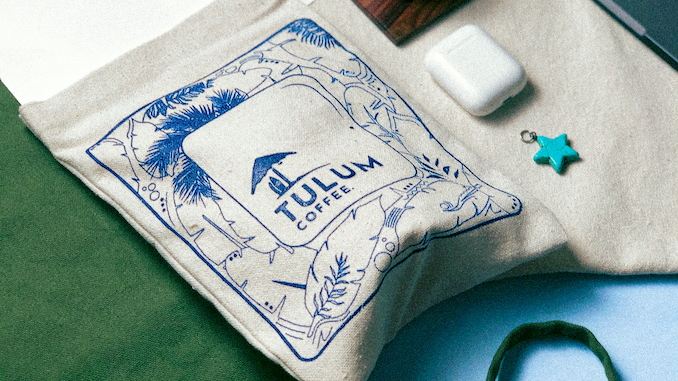 A bag of cloth holds coffee beans with the Tulum logo.