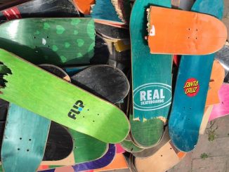 A handful of used colorful skateboards sitting in a pile on the floor.