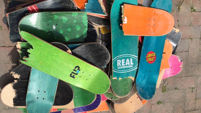 A handful of used colorful skateboards sitting in a pile on the floor.