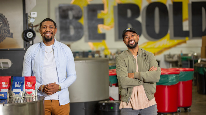 Rod and Pernell stand smiling with their arms crossed in their roastery, with their NBA bags sitting on a table in the corner.