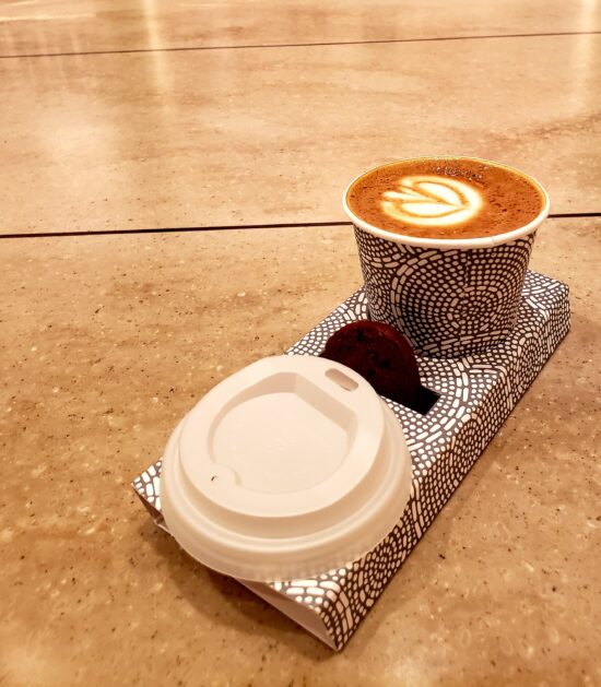 A coffee drink in a to-go carrier with a lid next to it.