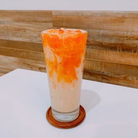 A creamsicle colored iced beverage with persimmon syrup atop milk, chilled in a glass.