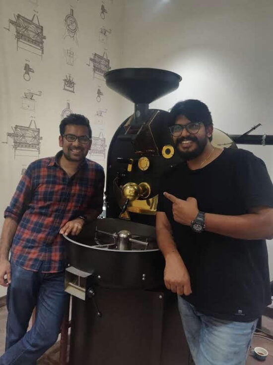 Binny Vargheses and Vaibhav Bindal pose by a coffee roaster.