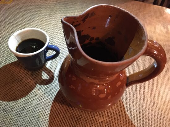 Una taza de café de olla junto a una jarra de barro.