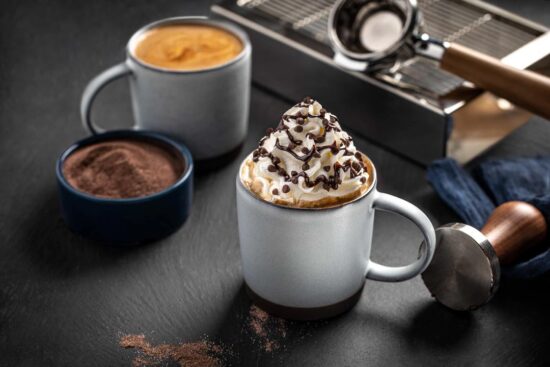 A mug filled a hot mocha drink and topped with a mountain of whipped cream and Ghirardelli chocolate.