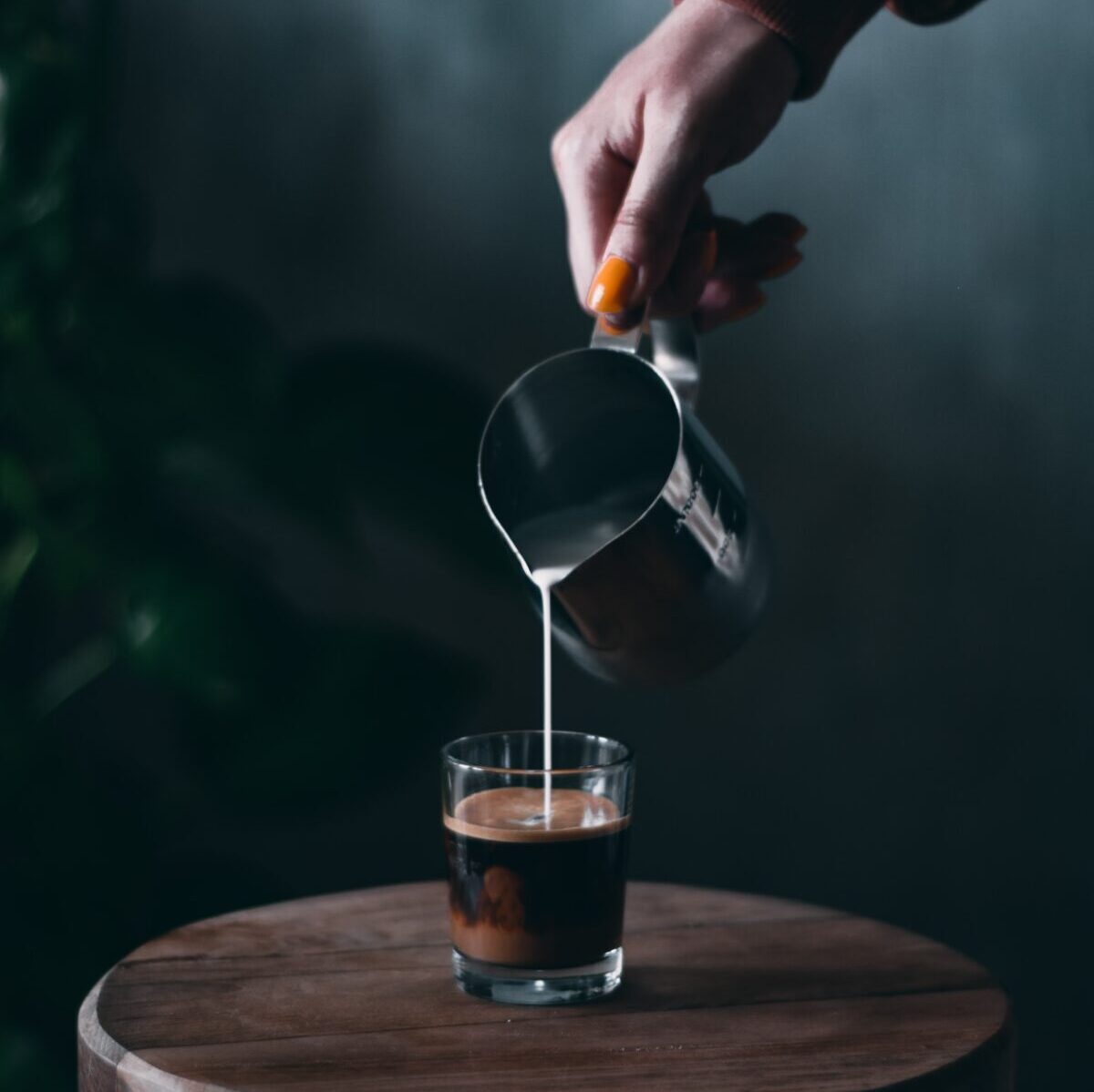 Barista naleje naparené mlieko z kovového džbánu do demitasse pohára naplneného do polovice espressom, aby vytvoril café con leche.