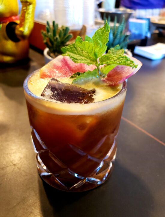 The rim of fire, a cold coffee drink in a double rocks glass, garnished with fresh mint leaves and pink watermelon radish.
