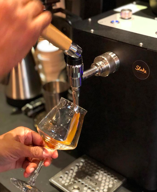 A barista pours nitro cold brew from a metal bar tap into a fluted glass similar to a wine glass.