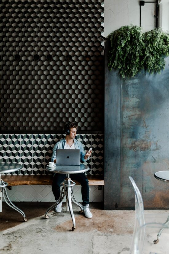 Uma pessoa sozinha em uma mesa de um café com um telefone e um laptop.
