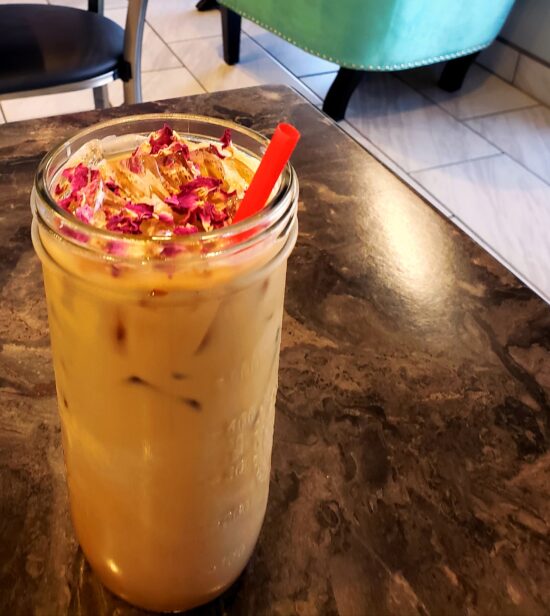 A cold milky concoction in a Mason jar with a red straw and topped with rose petals.