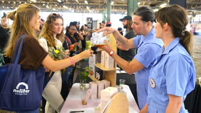 A man pours coffee from a glass pitcher into a small cup for a festival attendee.