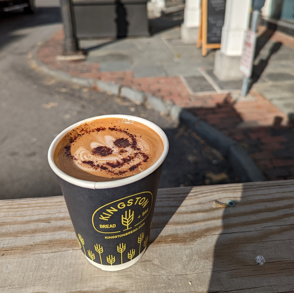 A spicy mocha in a paper cup from Kingston Bread and Bar. The top of the beverage features a skull stenciled in with cocoa topping.
