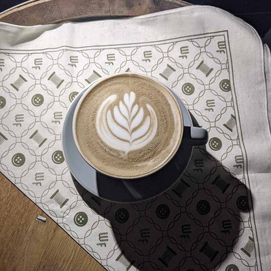 A latte in a lavender colored porcelain cup and saucer. Finished with a rosetta.