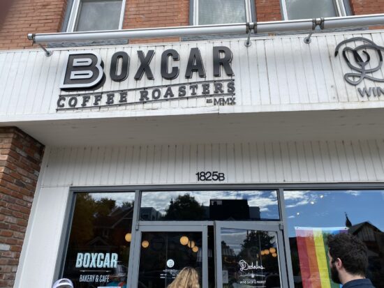 The wood paneled and glass exterior of Boxcar. There is a Pride flag in the window, otherwise the decor is black and white.