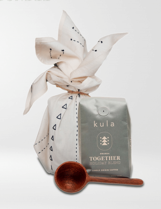 The Kula holiday bundle: a bag of coffee beans, a perfectly round coffee spoon made of hard word with a straight handle, and a white tea towel hand stitched with dashes and triangles