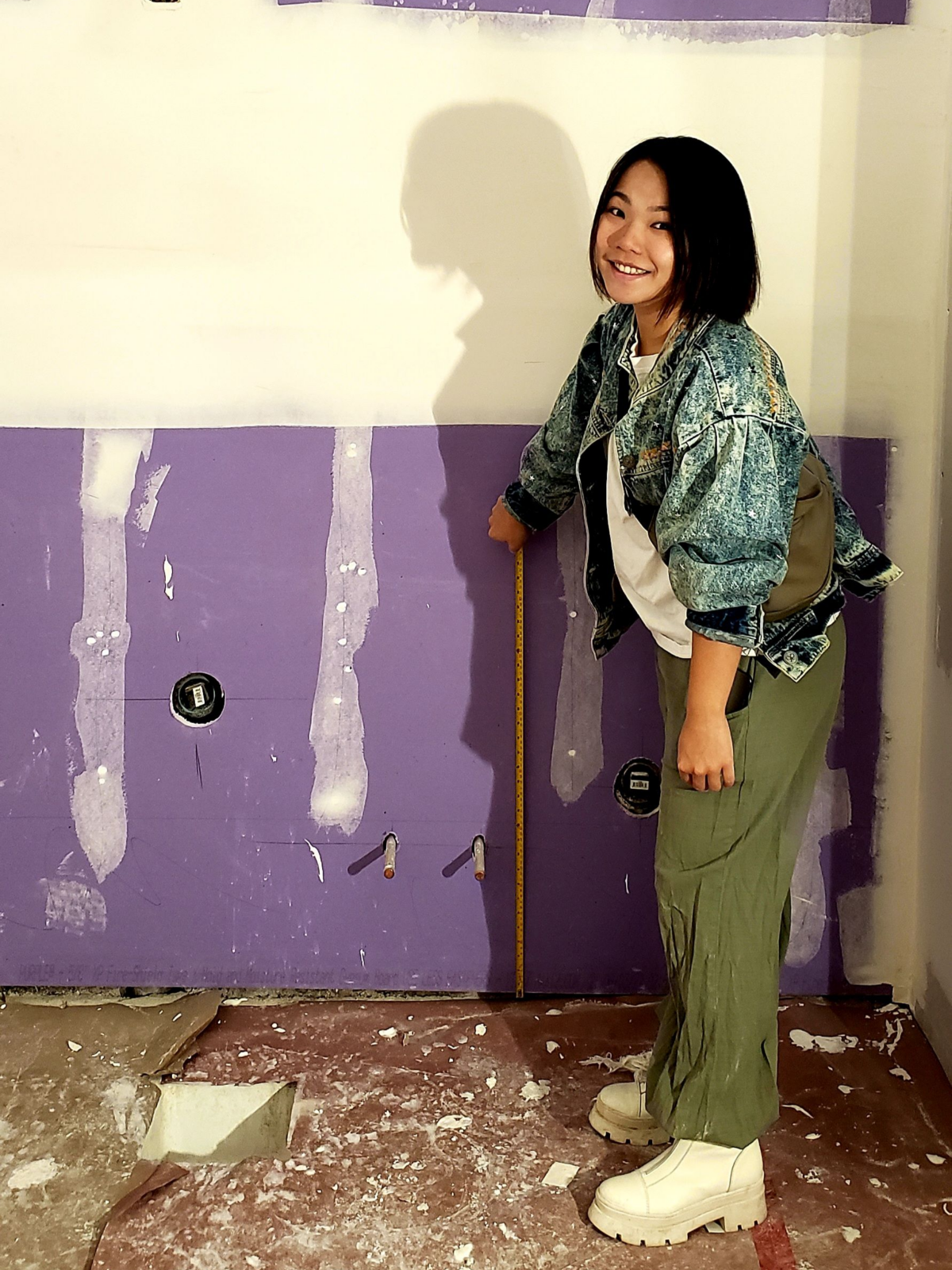 Owner Viviana holds a measuring tape up against a wall inside Mind Coffee. She wears white boots, army green pants, and an acid-washed loose denim jacket.