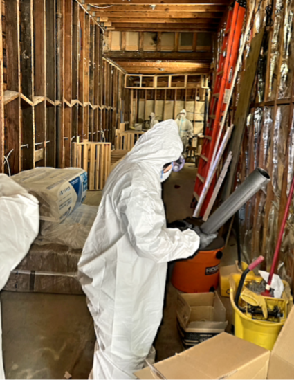 Workers in white safety suits and goggles work on building the Mind Coffee space. The wall studs are exposed, ladders lean against the walls, and assorted buckets and wood pallets are scattered inside.