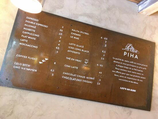 Café Piha's rustic metal menu sign features all sorts of coffee drinks, a coffee flight, and the words "let's go ride" all printed in white ink.