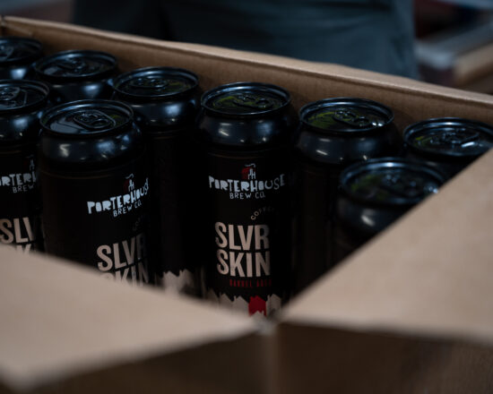 A cardboard box holding the black and silver cans of imperial coffee stout.