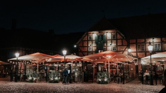 An outdoor market at night in Sweden. There are umbrellas and strings of electric lights clustered around Tudor style buildings, with greenery and snow on the ground.