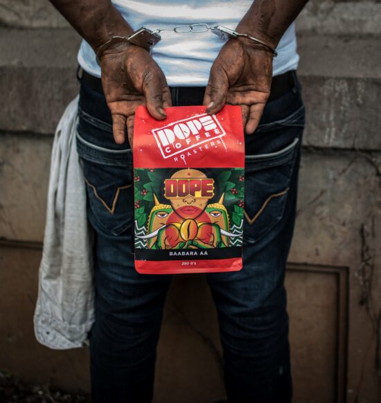 A mean in jeans has his hands behind his back in handcuffs. His hands are covered in dirt. He holds the same bag as above, and you can see a rag hanging from his pocket.