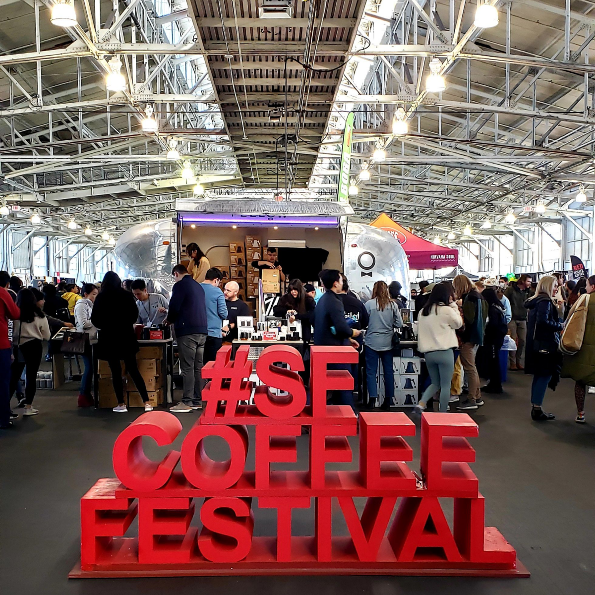 At the front of the huge pavilion is a big art stack of  bright red letters spelling out hashtag SF coffee festival in all caps.