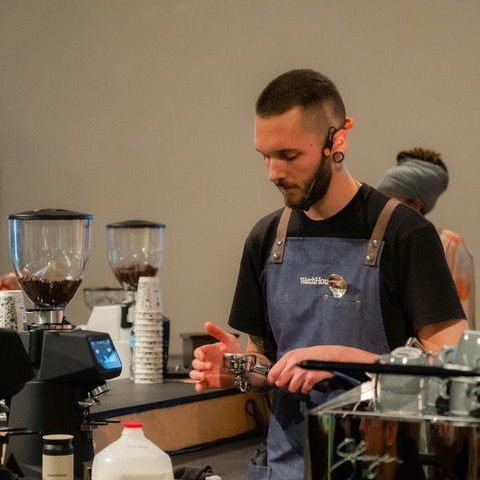 David has an espresso portafilter in his left hand and is tapping it with the other hand to settle the grounds.