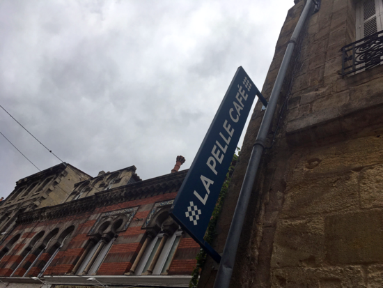 The blue La Pelle Café sign pokes out from a brick building with wrought iron window ledges,