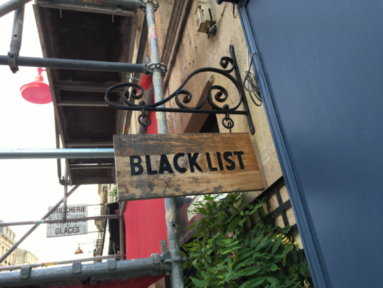 The metal and wood swinging sign outside Black List merely says the name in bold all caps black letters debossed on the wood.