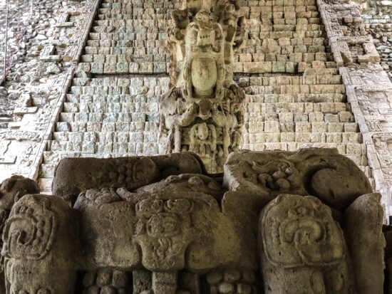 Izlizani kip boga ili svećenika na ruševinama Maja.  Čini se da u rukama drži posudu.  Nosi veliko pokrivalo za glavu od kamena i stoji na postolju s uskovitlanim motivima koji izgledaju poput zmija i voća.