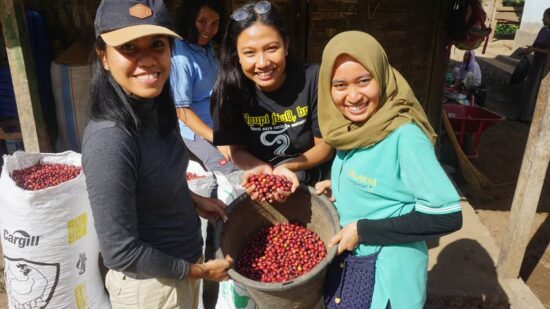Mahniwati of Kon Bayan Coffee and two other women hold up a big pot filled with red coffee cherries.