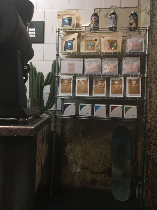 Butiksvæggen hos Motors byder på en høj kaktus, et skateboard og hylder med farverige kaffeposer, flasker og kasser til salg. 