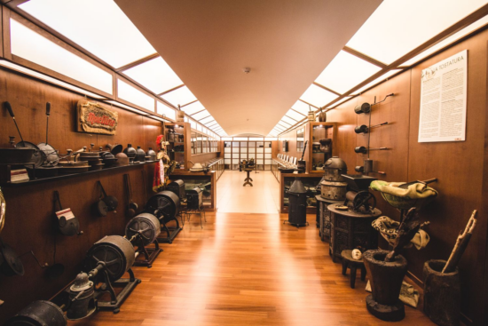 The interior of the coffee museum at Morettino headquarters. Along two wood-paneled walls are signs, bellows, old hand-turned coffee roasters, and all sorts of antique coffee roasting tools, mostly made of metal.