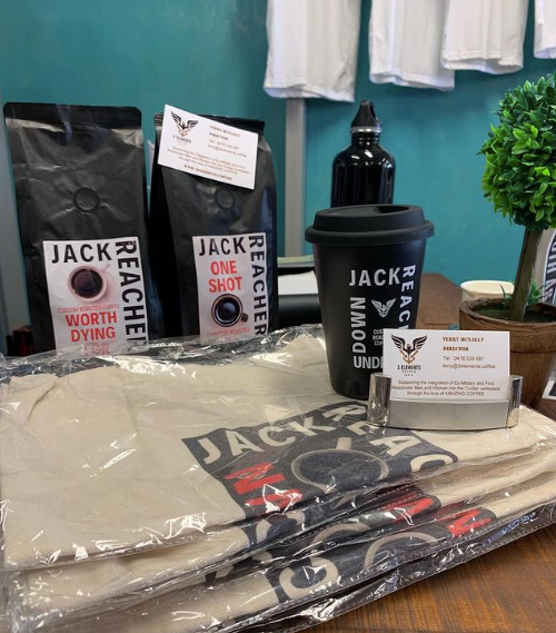 The line of Jack Reacher collab products. Two bags of coffee, one called Worth Dying For and the other One Shot, an all black travel mug with the words Down Under, a similar water bottle, and logo tote bags. 