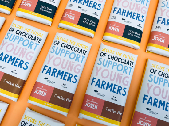 Retail wrapped coffee bars. They say "Secure the future of of chocolate. support young farmers." The bars are wrapped in white paper with yellow and pink and brown accents. 