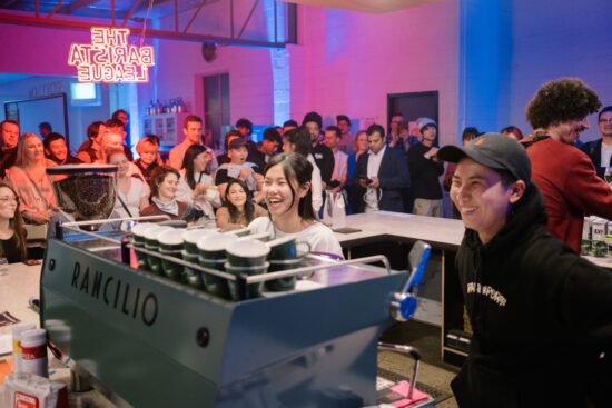 Two baristas behind a Rancilio espresso machine laugh during the competition.