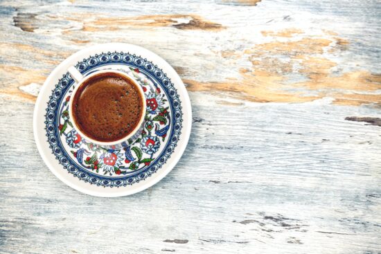 A wooden table top with an overhead view of a Turkish coffee in a traditional painted cup and saucer.