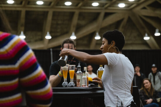 A barista/bartender pours a yellow cocktail in a fluted glass for the Coffee in Good Spirits contest, with onlookers in the background.