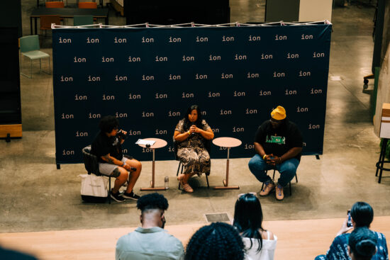 Three panelists, all BIPOC, two women and one man, sit in front of an audience at the 2022 event.