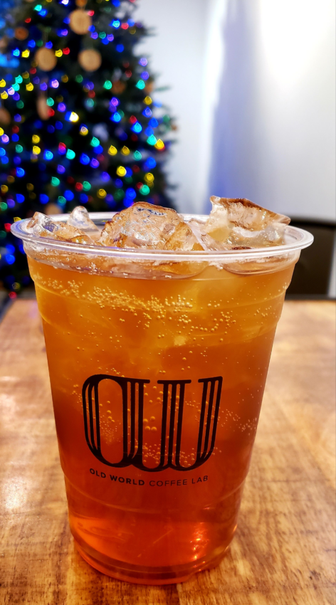 An old world coffee lab plastic cup with a fizzy drink inside, and a Christmas tree lit up in the background.