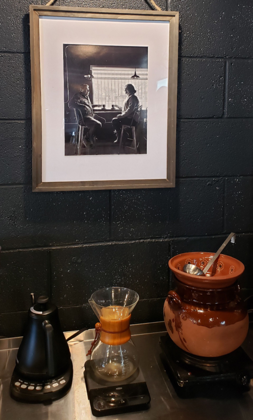 Inside the cafe is a black and white photo portrait of the owner's parents seated together with coffee at a counter. Below is a brewed pot of Café de Olla and a Chemex.