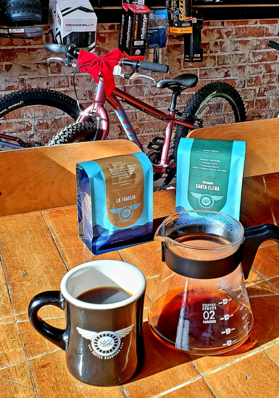 A mug and coffee server on a patio outside, with two coffee bags and a bike in the background.