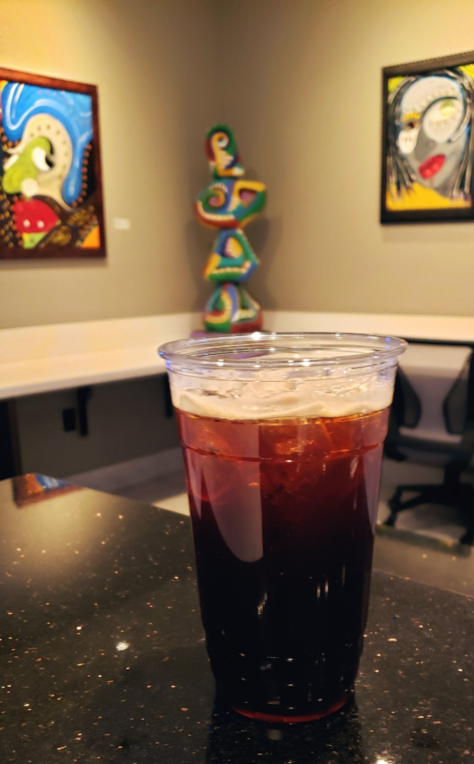 A fizzy Red Bull sparkling espresso drink in a plastic cup, with colorful artwork in the corner of the room.