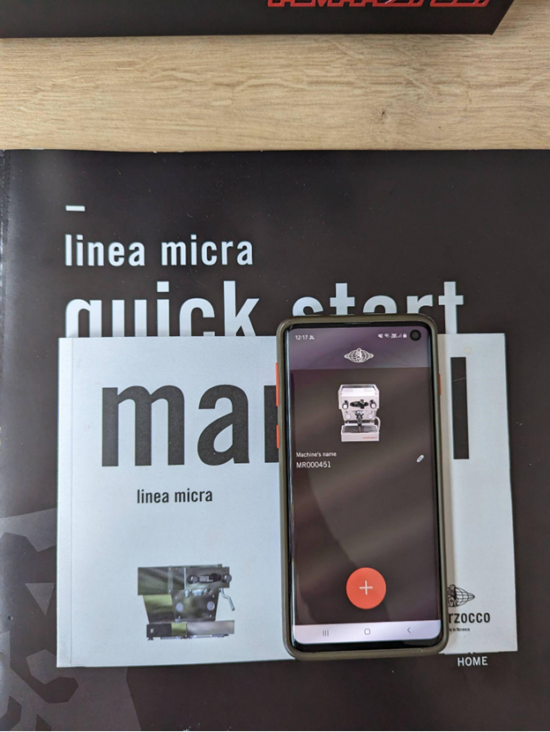 A photo of the Linea Micra start guide and manual and a cell phone sitting on top of it, with the La Marzocco Home App pulled up on the screen.