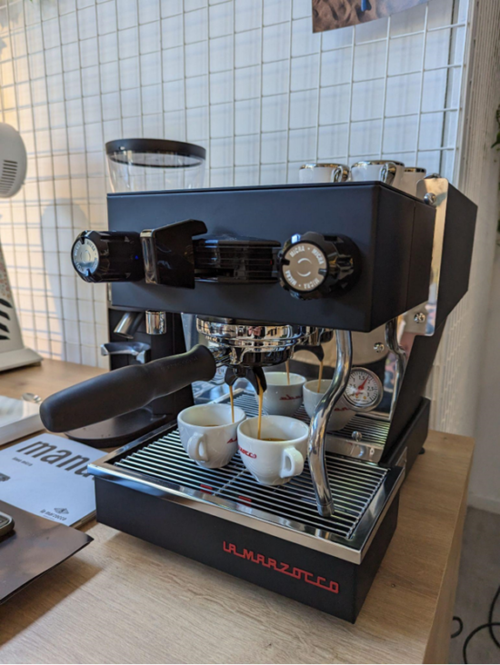 The Linea Micra pulls espresso shots. Two white cups are being filled with shots from the single grouphead, which can accomodate different types of shots. There are two knobs on the machine, one on each side: one pours hot water on the left, the other steams milk on the right. The portafilter sits in the middle. The top is flat so it can store ceramic cups.