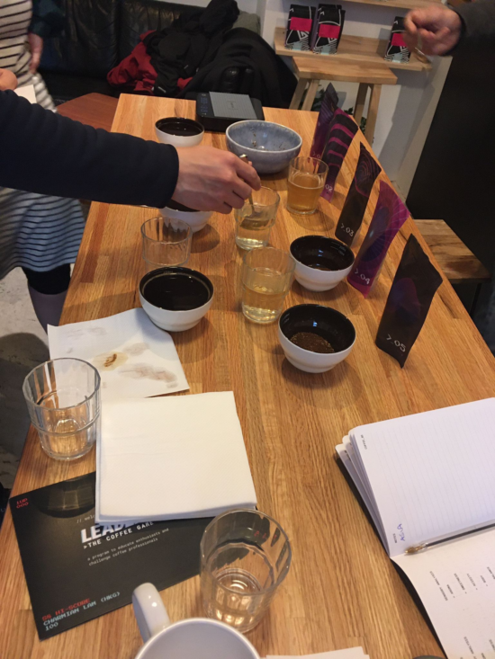 Players hold cupping spoons, tasting coffees as they go and making notes.