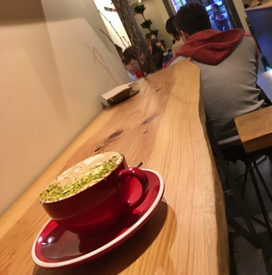 A red cermic cup and saucer holds the pistachio latte at Naji, which has a dusting of ground pistachio on top.
